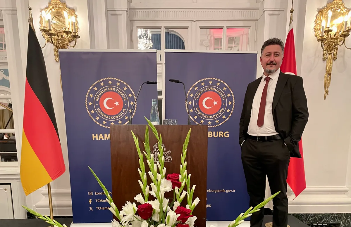 Resepsiyon sahnesinde Türk ve Alman bayraklarının yanında bir davetli.