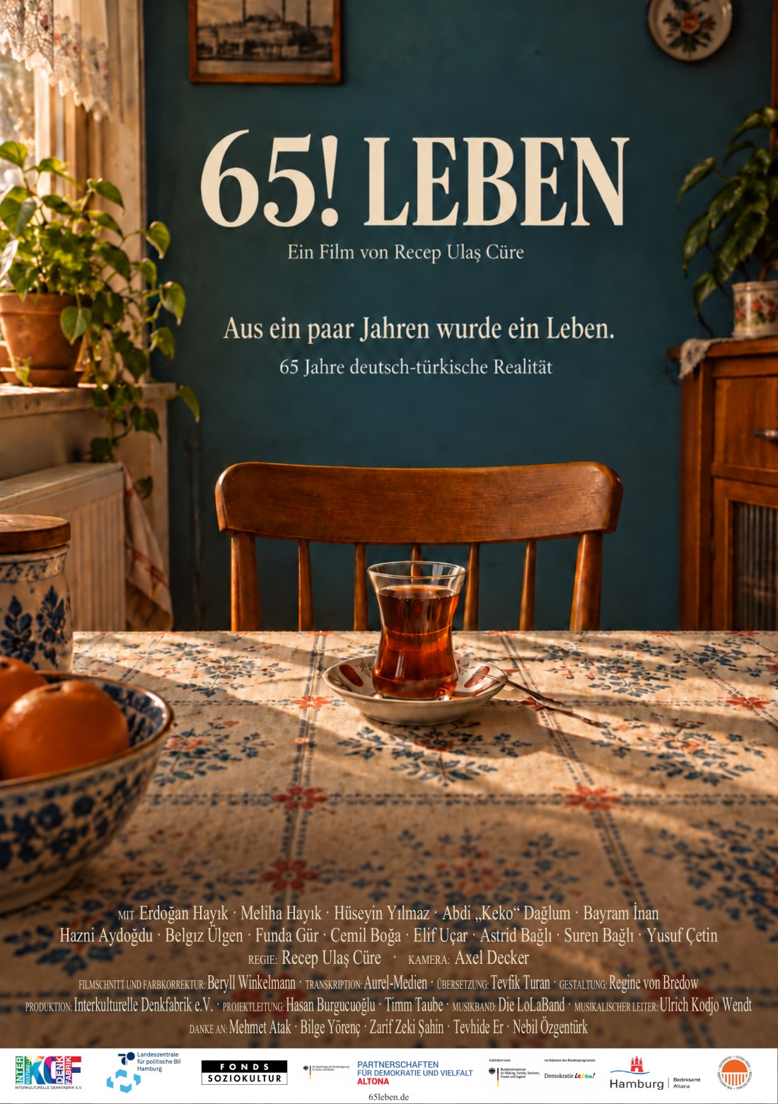 65! LEBEN film afişinde çay bardağı bulunan bir masa, boş sandalye ve mavi duvar.